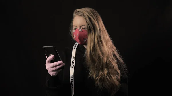 Menina com uma fita branca e a inscrição covid 19 em máscara vermelha leva selfie no smartphone. Isolado em fundo preto. Cuidados de saúde e conceito médico. Epidemia por Coronavírus — Fotografia de Stock
