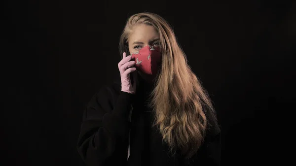 Дівчинка з білою стрічкою і напис covid 19 в червоній масці робить сельфі на смартфоні. Розташований на чорному тлі. Медична концепція та медична концепція. Епідемія коронавірусу — стокове фото