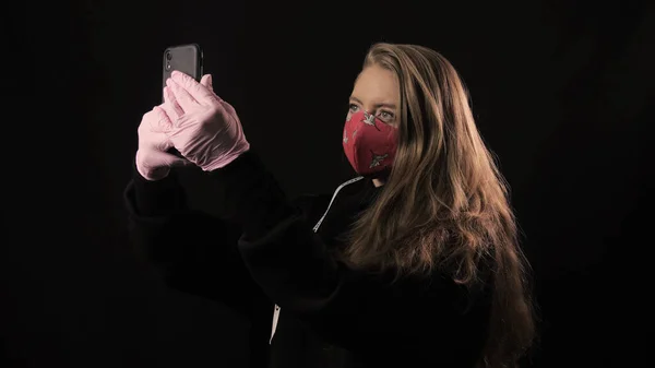 Дівчинка з білою стрічкою і напис covid 19 в червоній масці робить сельфі на смартфоні. Розташований на чорному тлі. Медична концепція та медична концепція. Епідемія коронавірусу — стокове фото