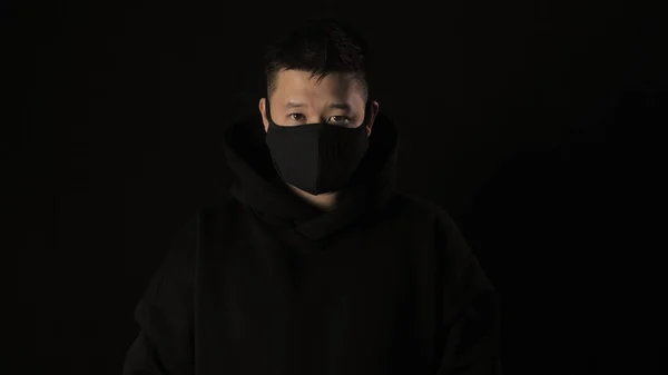 Asiático hombre en un negro médico máscara de coronavirus en un negro fondo con blanco cinta covid 19 — Foto de Stock