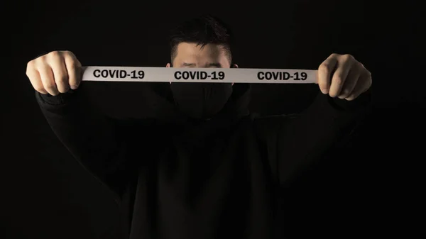 Asian man in a black medical mask from coronavirus on a black background with white tape covid 19 — Stock Photo, Image