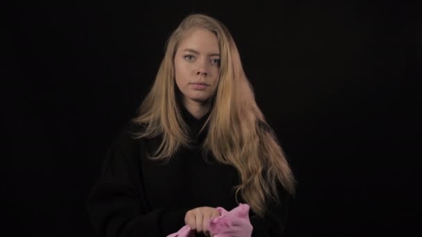 Mujer joven con el pelo dorado se pone guantes médicos de color rosa. Aislado sobre fondo negro. Salud y concepto médico. Cierre el retrato. 4k. Coronavirus Epidemia, enfermedad, pandemia — Vídeos de Stock