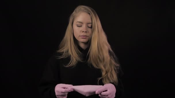 Une jeune femme avec des gants roses met un masque médical rose. Isolé sur fond noir. Soins de santé et concept médical. Gros plan portrait. 4k. Coronavirus Épidémie, maladie, pandémie — Video