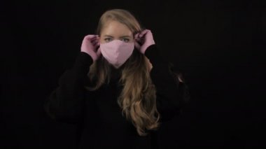 Kız önce pembe bir tıbbi maske takıyor, sonra da siyah bir maskenin üstüne. Siyah arka planda izole edilmiş. Sağlık ve tıbbi konsept. Portreyi kapat. 4 bin. Coronavirus Salgını, Hastalık, Salgın