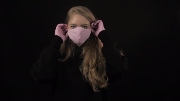 Dívka si nasadí růžovou lékařskou masku a pak si nasadí černou masku. Izolované na černém pozadí. Zdravotní péče a lékařská koncepce. Zavřít portrét. 4k. Koronavirus Epidemie, onemocnění, pandemie — Stock video
