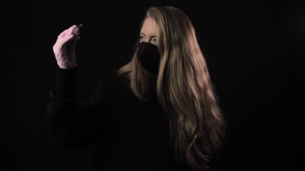 Chica con una máscara negra sostiene un tubo de ensayo con sangre y la inscripción covid-19. Aislado sobre fondo negro. Salud y concepto médico. Epidemia del Coronavirus — Vídeo de stock