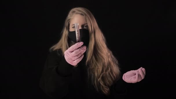 Flicka i svart mask håller ett provrör med blod och inskriptionen covid-19. Isolerad på svart bakgrund. Sjukvård och medicinskt koncept. Epidemi med coronavirus — Stockvideo