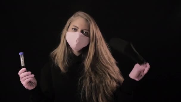 핑크 마스크를 쓴 소녀는 피가 묻어 있는 시험관을 들고 있다. 검은 배경에 고립되어 있습니다. 건강 관리와 의학 개념. 코로나 바이러스 유행병 — 비디오