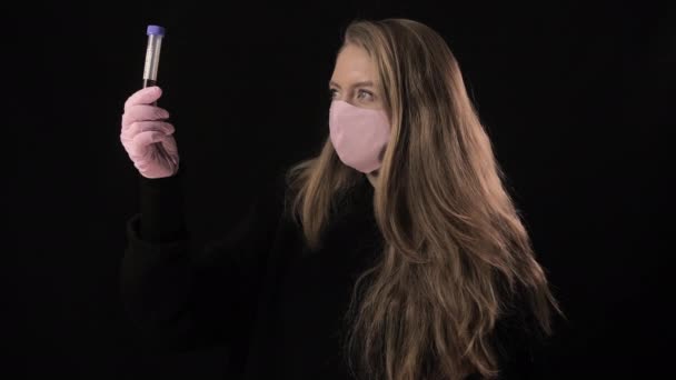 Дівчинка в рожевій масці тримає пробірку з кров'ю і написом covid-19. Розташований на чорному тлі. Медична концепція та медична концепція. Епідемія коронавірусу — стокове відео