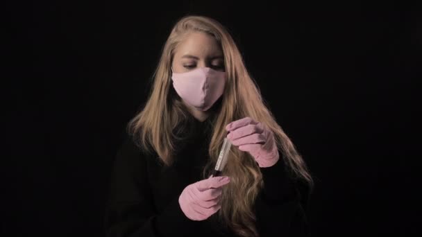 Κορίτσι με ροζ μάσκα κρατά ένα δοκιμαστικό σωλήνα με αίμα και η επιγραφή covid 19 ανοίγει και βήχει... απομονωμένη σε μαύρο φόντο. Ιατρική περίθαλψη και ιατρική έννοια. Επιδημία του Coronavirus — Αρχείο Βίντεο