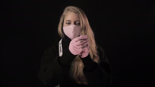 Flicka med vit tejp covid-19 tar av sig sina rosa handskar och rosa medicinsk mask och börjar hosta. Isolerad på svart bakgrund. Sjukvård och medicinskt koncept. Epidemi med coronavirus — Stockvideo