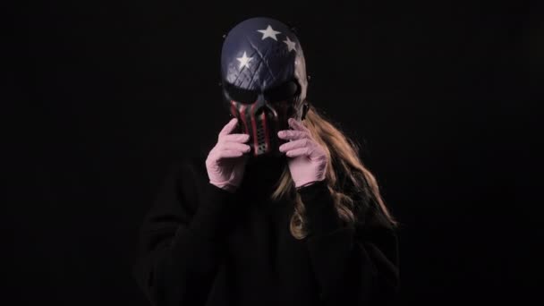 Dziewczyna zdejmuje straszną maskę USA, a pod nią różowa maska medyczna. Odizolowany na czarnym tle. Opieka zdrowotna i koncepcja medyczna. Zamknij portret. 4k. Koronawirus Epidemia, choroba, pandemia — Wideo stockowe