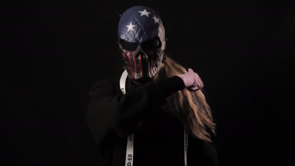 Meisje in een eng USA kleurenmasker en een wit lint met de inscriptie covid 19 toont een gebaar van de dood. Geïsoleerd op zwarte achtergrond. Gezondheidszorg en medisch concept. Coronavirus Epidemisch — Stockvideo