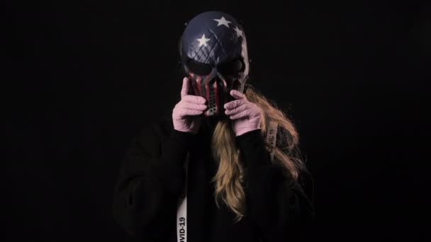 Dziewczyna zdejmuje straszną maskę USA, a pod nią różowa maska medyczna. Odizolowany na czarnym tle. Opieka zdrowotna i koncepcja medyczna. Zamknij portret. 4k. Koronawirus Epidemia, choroba, pandemia — Wideo stockowe