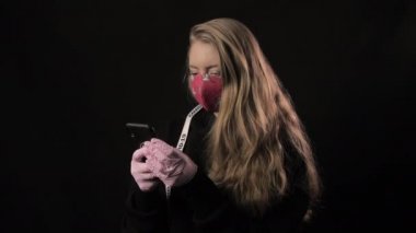 Beyaz kurdeleli ve kırmızı maskeli Covid 19 yazılı kız akıllı telefondan selfie çekiyor. Siyah arka planda izole edilmiş. Sağlık ve tıbbi konsept. Koronavirüs salgını