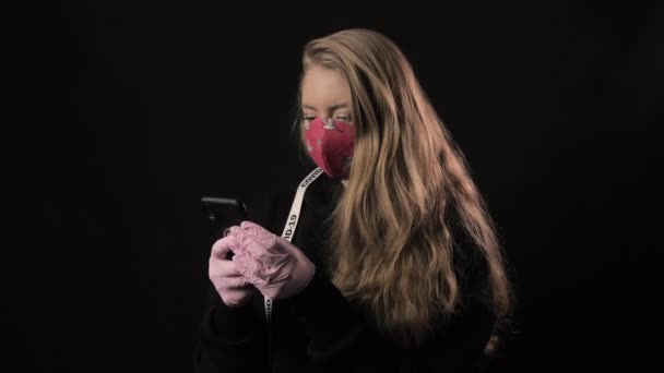 Menina com uma fita branca e a inscrição covid 19 em máscara vermelha leva selfie no smartphone. Isolado em fundo preto. Cuidados de saúde e conceito médico. Epidemia por Coronavírus — Vídeo de Stock