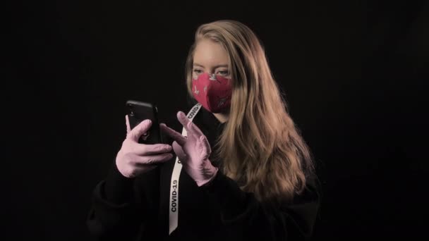 Fille avec un ruban blanc et l'inscription covid 19 en masque rouge prend selfie sur smartphone. Isolé sur fond noir. Soins de santé et concept médical. Épidémie de coronavirus — Video