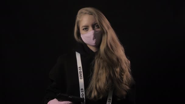 Κορίτσι κρατά όπλο και λευκή ταινία επιγραφή covid 19. Απομονωμένο σε μαύρο φόντο. Ιατρική περίθαλψη και ιατρική έννοια. Κοντινό πορτραίτο. 4k. Επιδημία του Coronavirus — Αρχείο Βίντεο