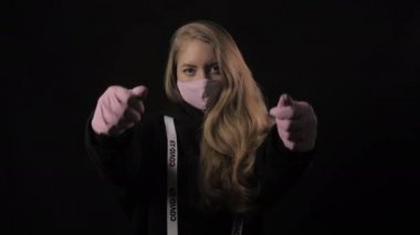 Girl in a pink mask and a ribbon with the inscription covid 19 show gesture Fuck. Isolated on black background. Health care and medical concept. Close up portrait . 4k. Coronavirus Epidemic