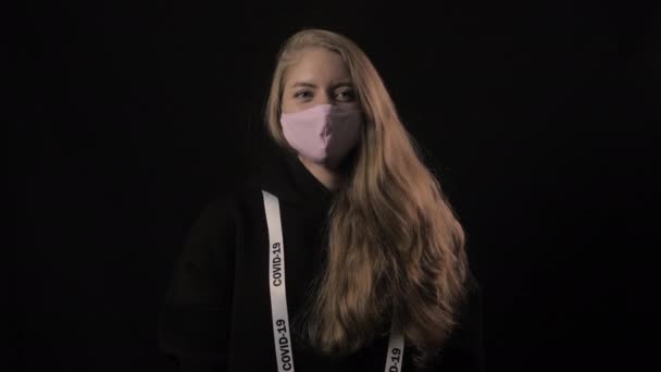 Flicka i rosa mask och band med inskriptionen covid 19 skratt. Isolerad på svart bakgrund. Sjukvård och medicinskt koncept. Närbild porträtt. 4k. Epidemi med coronavirus — Stockvideo