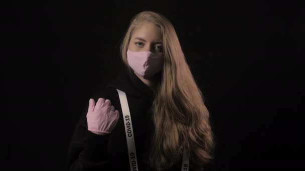 Дівчина в рожевій масці і стрічка з написом ковадла 19 показують жест Нахрен. Ізольовані на чорному тлі. Охорона здоров'я та медична концепція. Портрет крупним планом. 4k. епідемія коронавірусу — стокове відео