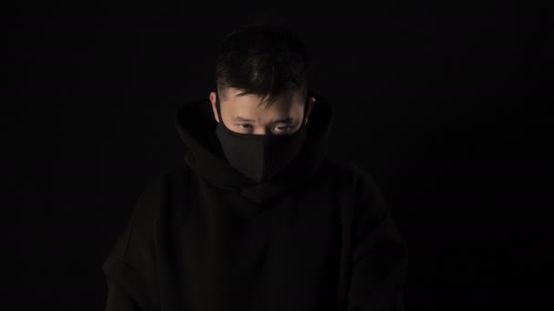 Азіатський чоловік у чорній медичній масці з коронавірусу на чорному тлі з білою стрічкою covid 19 — стокове відео