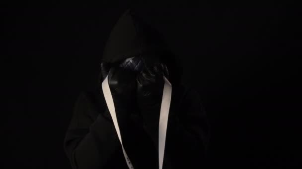 Человек в страшной маске держит белую ленту с надписью covid 19. Изолированный на черном фоне. Здравоохранение и медицинское понятие. Эпидемия коронавируса, болезни, пандемия. Маска США — стоковое видео