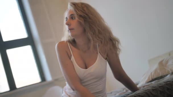 Menina sexy em um top tanque branco e calções jeans curtos azuis deitado na cama — Vídeo de Stock