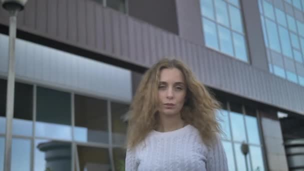 Chica en un suéter blanco con una mirada triste se encuentra en el fondo de un edificio de negocios — Vídeos de Stock