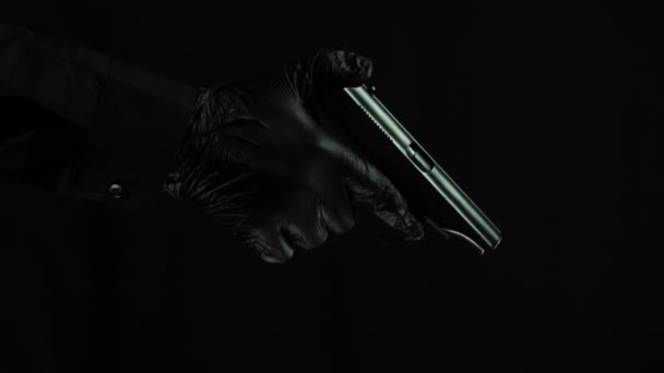 Чоловіча рука в чорних рукавичках завантажує пістолет на чорному тлі — стокове відео