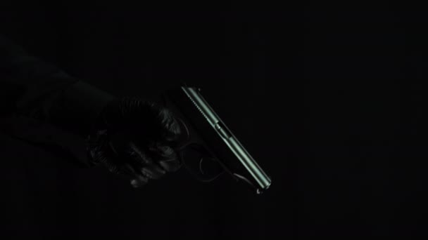 Мужская рука в черных перчатках заряжает пистолет на черном фоне — стоковое видео
