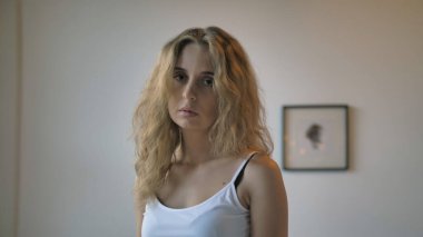 Beyaz atletli seksi bir kız ve açık renkli bir duvarın önünde duran mavi kısa kot şortlu.