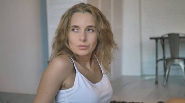 Beyaz kolsuz tişörtlü, mavi şortlu, yatakta oturan ve yan tarafa bakan seksi kız.