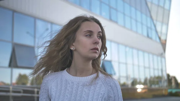 Mädchen im weißen Pullover mit traurigem Blick steht vor dem Hintergrund eines Geschäftshauses — Stockfoto