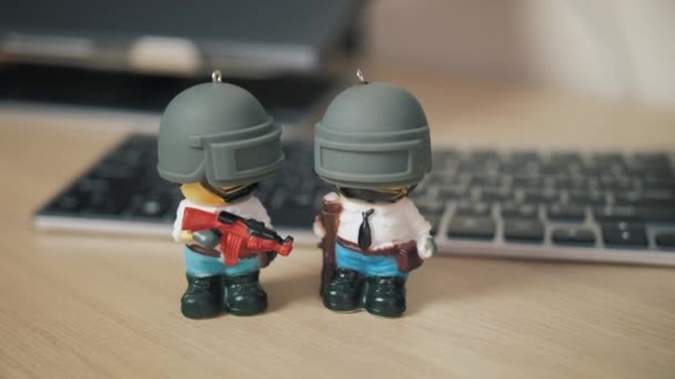 Два маленьких человечка из игры PUBG с винтовкой стоят на столе на фоне ноутбука и беспроводной клавиатуры — стоковое видео