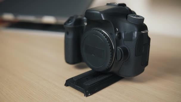 Uma câmera preta sem uma lente com uma placa destacável rápida está em uma mesa de madeira — Vídeo de Stock