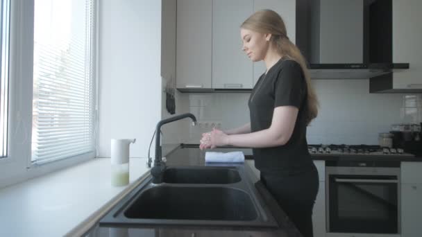 Девушка в черной одежде моет руки с мылом на кухне — стоковое видео