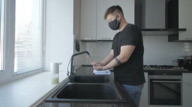 Siyah tişörtlü ve kot pantolonlu Asyalı adam mutfakta sabunla ellerini yıkıyor.