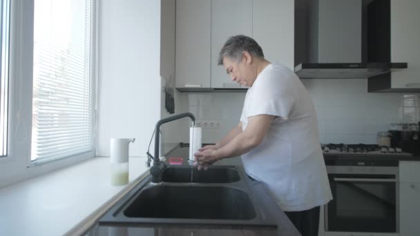 Азиатский старик в белой футболке моет руки с мылом на кухне кистью — стоковое видео