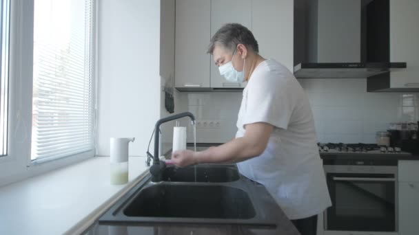 Asiatisk gammal man med mask i vit t-shirt tvättar händerna med tvål i köket med pensel — Stockvideo