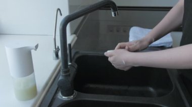 Kadın mutfakta fırçayla ellerini sabunla yıkıyor.