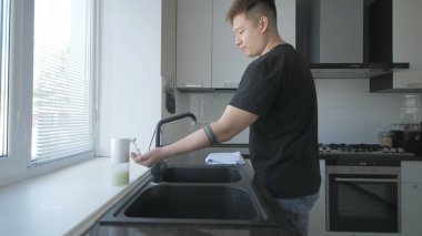 Siyah tişörtlü ve kot pantolonlu Asyalı adam mutfakta sabunla ellerini yıkıyor.