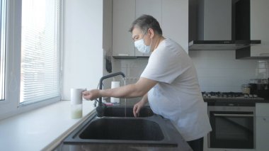 Beyaz tişörtlü Asyalı yaşlı adam mutfakta sabunla ellerini yıkıyor.