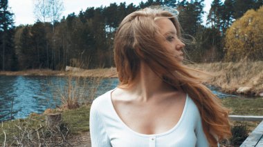 Güzel sarışın kadın gölün yakınındaki bir parkta oturup dinleniyor. Yan görünüm