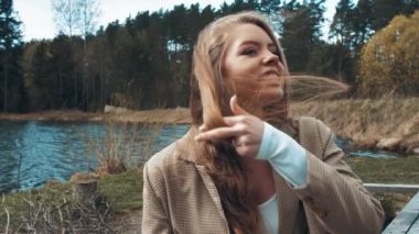 Güzel sarışın kadın gölün yakınındaki bir parkta oturup dinleniyor. Yan görünüm