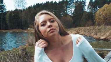 Güzel sarışın kadın gölün yanındaki parkta oturuyor ve daha güzel. Ön görünüm