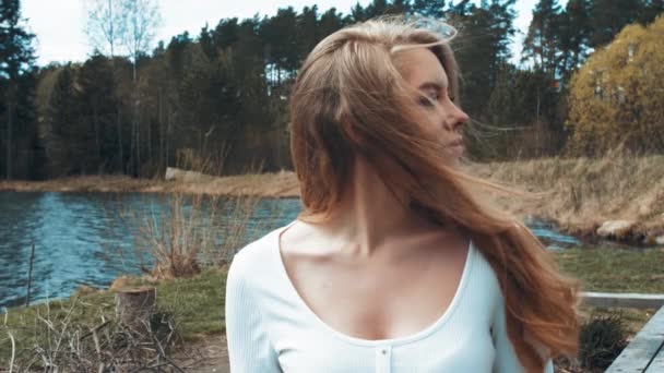 Hermosa joven rubia sentada y relajarse en un parque cerca del lago. Vista lateral — Vídeos de Stock