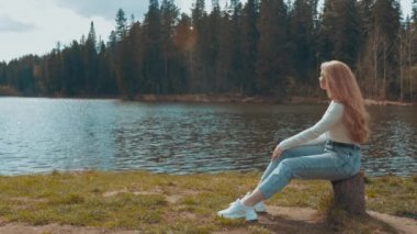 Güzel sarışın kadın gölün yakınındaki bir parkta oturup dinleniyor. Yan görünüm