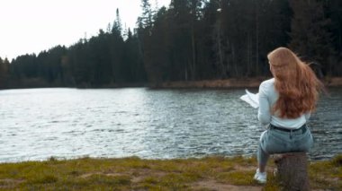 Güzel sarışın kadın gölün yanındaki parkta oturmuş kitap okuyor. Arka plan