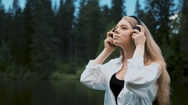 TOMSK, RÚSSIA - Maio 23, 2020: Mulher loira jovem bonita com aparência natural ouvir música em preto sony WH 1000xm3 fones de ouvido — Fotografia de Stock